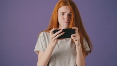 Mutlu genç bir kadın akıllı telefonuyla oyun oynuyor menekşe arka planda yalnız duruyor.