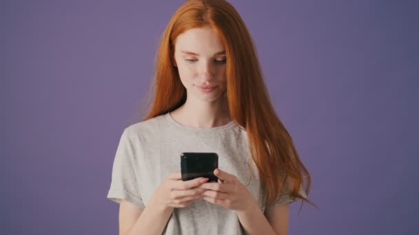 Een Geconcentreerde Jonge Vrouw Gebruikt Haar Smartphone Geïsoleerd Een Violette — Stockvideo