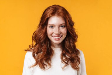 Kızıl, neşeli, gülümseyen ve sarı arka planda izole edilmiş kameraya bakan bir kız görüntüsü