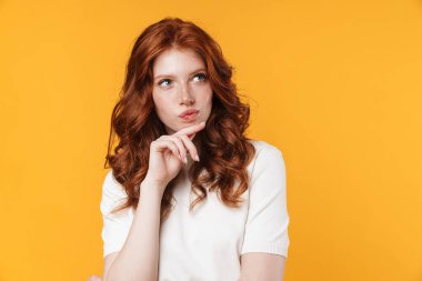 Kızıl ciddi bir kızın sarı arka planda izole edilmiş bir şekilde düşünmesi ve bakması.