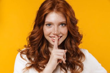 Kızıl, neşeli kızın sarı arka planda izole edilmiş sessizlik jesti görüntüsü