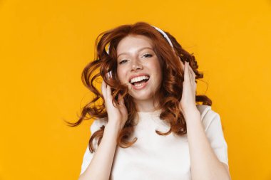 Kızıl saçlı heyecanlı kızın sarı arka planda izole edilmiş kulaklık kullanması.