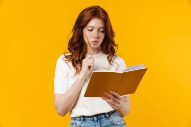 Kızıl, ciddi bir kızın sarı arka planda izole edilmiş egzersiz kitabını tutması.