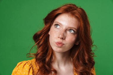 Kızıl, ciddi bir kızın sarı arka planda izole edilmiş ve yukarı bakan görüntüsü.