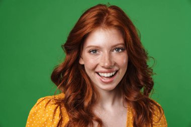 Kızıl, neşeli, gülümseyen ve yeşil arka planda izole edilmiş kameraya bakan bir kız görüntüsü