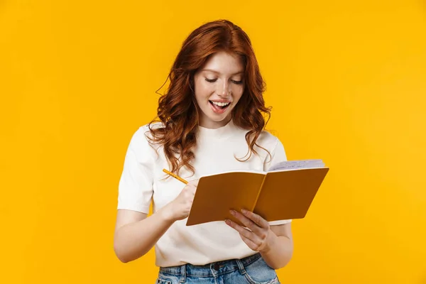 Afbeelding Van Gember Vrolijk Meisje Schrijven Oefenboek Geïsoleerd Gele Achtergrond — Stockfoto