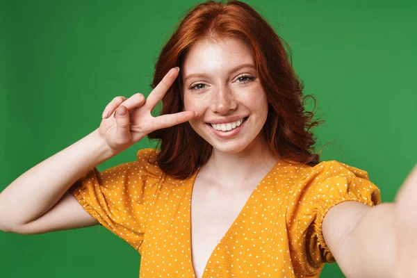 赤い頭の陽気な女の子が平和サインをジェスチャーし 緑の背景に隔離された写真を撮るイメージ — ストック写真