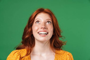 Kızıl, neşeli, gülümseyen ve yeşil arka planda izole bir şekilde yukarıya bakan kız görüntüsü.