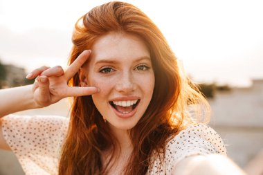 Şehir caddesinde selfie çekerken barış işareti yapan neşeli kızıl kız görüntüsü