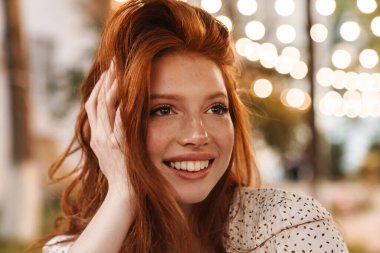 Şehirli caddede gülümseyen ve kameraya bakan neşeli kızıl kız görüntüsü