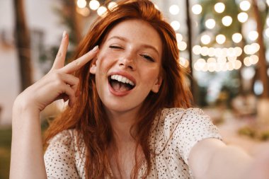 Şehir caddesinde selfie çekerken barış işareti yapan neşeli kızıl kız görüntüsü