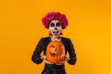 Cadılar Bayramı makyajlı beyaz kız sarı arka planda balkabağıyla poz veriyor.