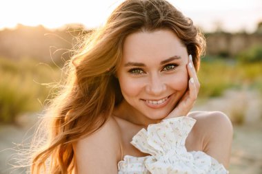 Beyaz tenli çekici esmer kadın gülümsüyor ve dışarıda kameraya bakıyor.