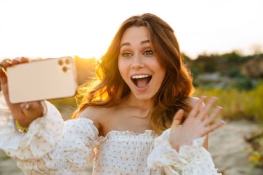 Beyaz tenli çekici esmer kadın gülümsüyor ve cep telefonuyla selfie çekiyor.