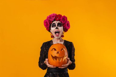 Cadılar Bayramı makyajlı beyaz kız sarı arka planda balkabağıyla poz veriyor.