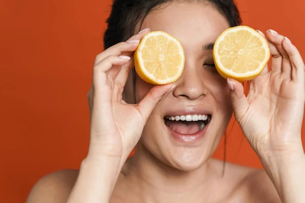 オレンジ色の背景の上にレモンで隔離されたポーズをしながら笑う恥知らずなアジアの女の子のイメージ — ストック写真