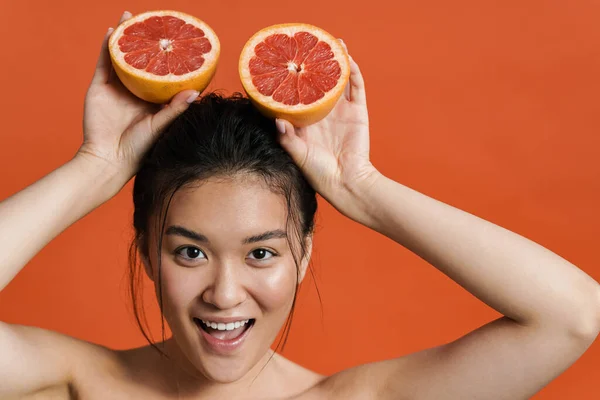 明るいトップレス若いアジアの女性の美しさの肖像画は オレンジの背景に孤立立っている間ポーズ カットグレープフルーツを保持 — ストック写真