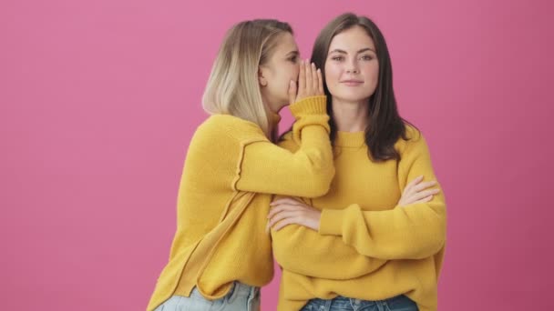 Dos Mujeres Sonrientes Con Suéteres Amarillos Comparten Secretos Aislados Sobre — Vídeos de Stock