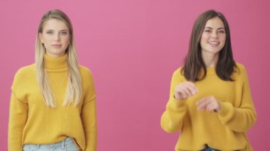 İki mutlu kız birbirini işaret ediyor. Stüdyoda pembe arka planda izole bir şekilde duruyorlar.