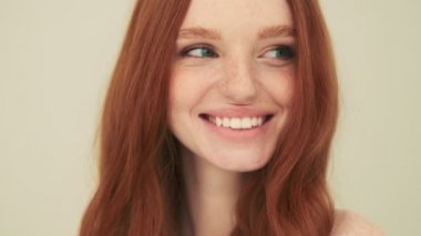 Çekici bir kadının yakın plan görüntüsü gülümsüyor. Stüdyoda bej arka planda tek başına duruyor.