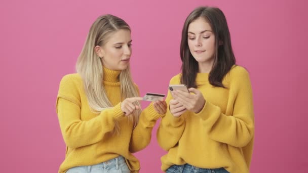 Lachende Vrouwen Gebruiken Credit Card Smartphone Staan Geïsoleerd Roze Achtergrond — Stockvideo