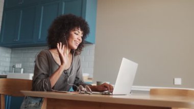 Gülümseyen Afrikalı kadın evde oturmuş video konuşmalarıyla dizüstü bilgisayar kullanıyor.