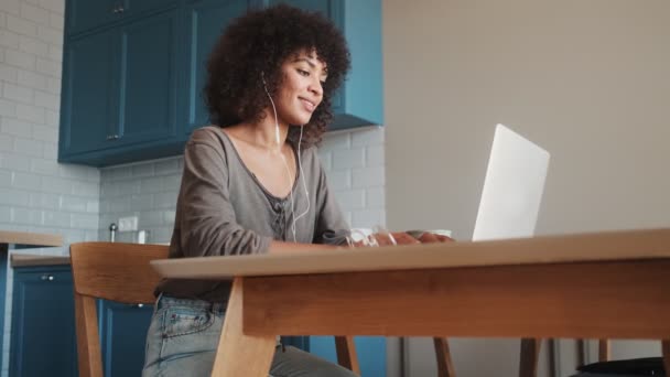 快乐的非洲女人坐在家里 一边用手提电脑一边听音乐一边用耳机听音乐 — 图库视频影像