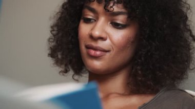 Gülümseyen konsantre Afrikalı kadın evde kitap okuyor.