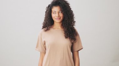 Rüya gören Afrikalı Amerikalı bir kadın kameraya poz veriyor. Bej arka planda tek başına duruyor.