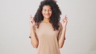 Olumlu bir Afro-Amerikan kadını, bej arka planda tek başına dikilirken dilek diliyor.