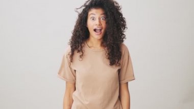 Mutlu bir Afrikalı Amerikalı kadın, bej arka planda tek başına ayakta alkışlıyor ve seviniyor.