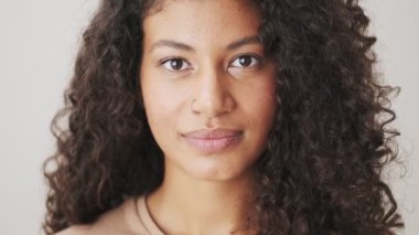 Şaşırmış bir Afrikalı Amerikalı kadının yakın çekim görüntüsü bej arka planda tek başına duran kameraya bakıyor.