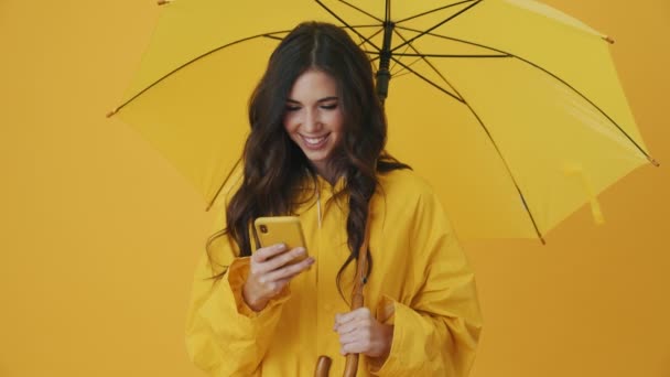 Una Mujer Sonriente Está Usando Teléfono Inteligente Mientras Sostiene Paraguas — Vídeos de Stock