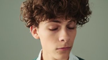 Çekici bir delikanlının yakın çekim görüntüsü stüdyodaki gri duvarın arkasında izole bir şekilde duran gizli bir jest yapıyor.