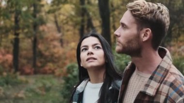 Genç bir çift, sonbahar parkında yürürken etrafa bakınıyorlar.