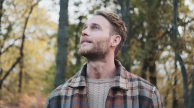 Gülümseyen bir adam sonbahar parkında yürürken etrafına bakıyor.