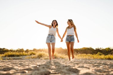 Dışarıda yürürken gülümseyen ve el ele tutuşan iki beyaz kadın.