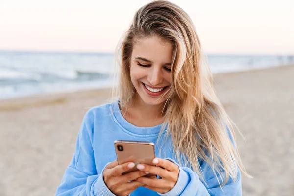 Joven Mujer Rubia Caucásica Sonriendo Sosteniendo Teléfono Celular Mientras Camina — Foto de Stock
