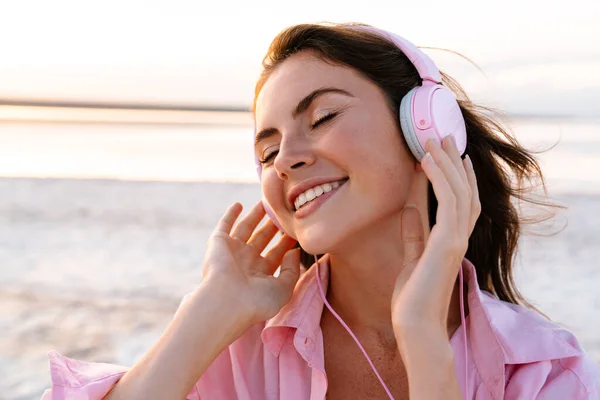 在海滩上 一个戴着太阳镜 戴着耳机听音乐的快乐小女孩的照片 — 图库照片