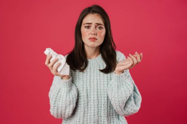 Grip olmuş, pembe arka planda peçete tutan mutsuz güzel bir kız resmi.