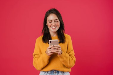 Pembe arka planda izole edilmiş gülümseyen ve cep telefonu kullanan neşeli esmer kız görüntüsü
