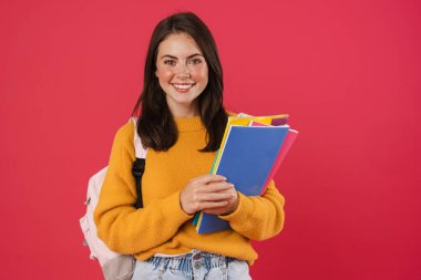 Pembe arka planda izole edilmiş egzersiz kitaplarıyla poz veren mutlu güzel kız öğrenci görüntüsü