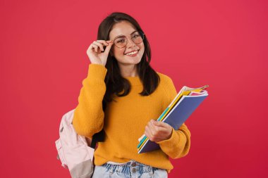 Pembe arka planda izole edilmiş egzersiz kitaplarıyla poz veren mutlu güzel kız öğrenci görüntüsü