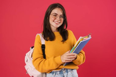 Pembe arka planda izole edilmiş egzersiz kitaplarıyla poz veren mutlu güzel kız öğrenci görüntüsü