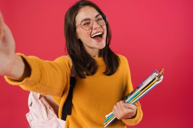 Egzersiz kitaplarıyla gülen bir kızın pembe arka planda izole edilmiş selfie çektiği bir resim.