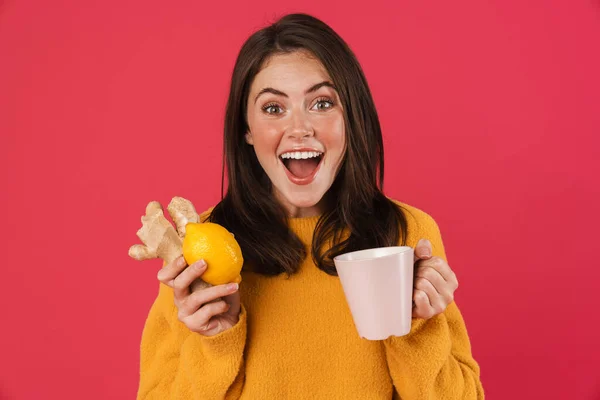 照片上兴奋的高加索女孩一边拿着柠檬和姜一边喝着粉色背景的茶 — 图库照片