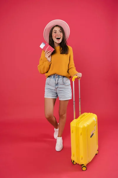 照片中兴奋的高加索女孩拿着手提箱和护照在粉色背景下摆姿势 — 图库照片