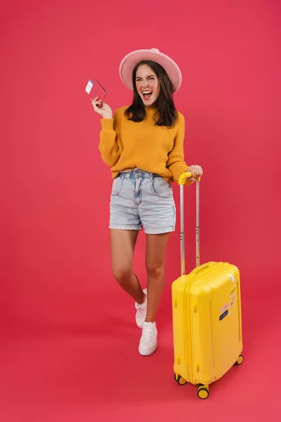 一个带着旅行袋走起路来的快乐的年轻女子 手里拿着护照和车票 背景是粉色的 — 图库照片