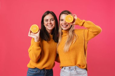 Pembe arka planda portakalla poz verirken sarılan neşeli kadınların görüntüsü