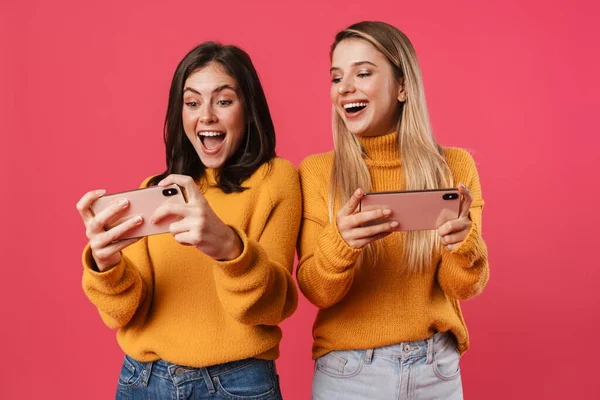 Две Счастливые Красивые Девушки Используя Мобильные Телефоны Изолированы Розовом Фоне — стоковое фото
